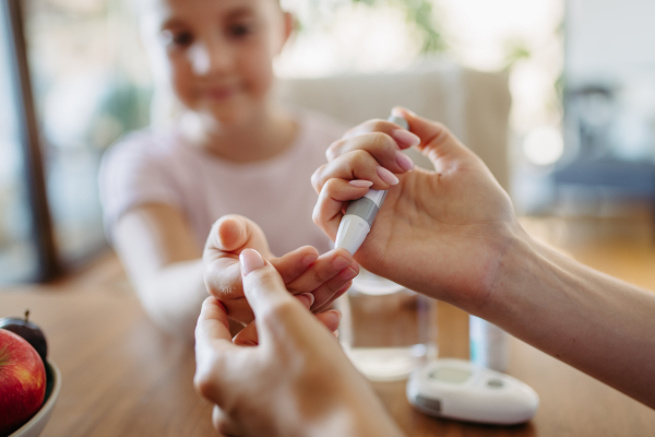 Close up of mother checking girl's blood glucose level using a fingerstick glucose meter. Endocrinologist waiting for results from blood test.