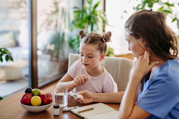 Mother checking girl's blood glucose level using a fingerstick glucose meter before meal. Diabetic girl waiting for results from blood test.