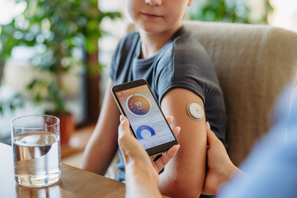 Girl with diabetes checking blood glucose level at home using continuous glucose monitor. Girl's mother connects CGM to a smartphone to monitor her blood sugar levels in real time.