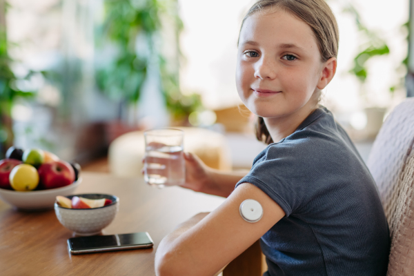 Close up of continuous glucose monitor sensor on girl's arm. Girl drinking water to better manage her diabetes.