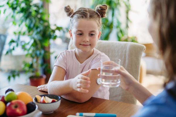 Diabetic girl drinking water to better manage her diabetes. Continuous glucose monitor sensor on diabetic girl's arm.