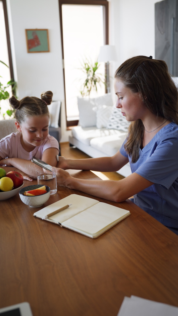 Girl with diabetes checking blood glucose level at home using continuous glucose monitor. Girl's mother connects CGM to a smartphone to monitor her blood sugar levels in real time.