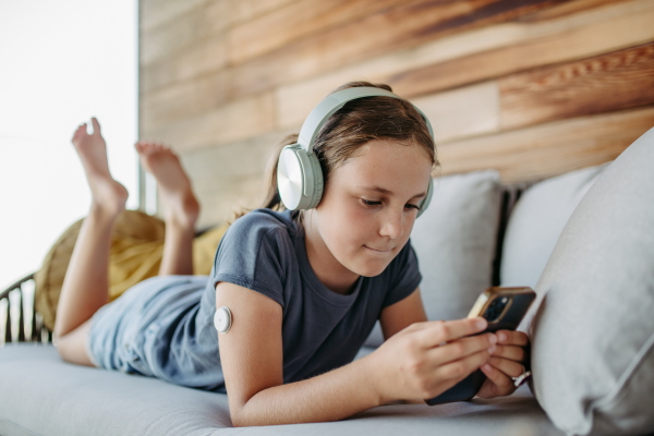 Diabetic girl watching social media content on smart phone.The CGM device makes the life of the schoolgirl. easier, helping manage her illness and focus on other activities.