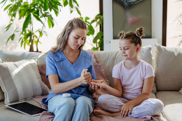 Nurse checking girl's blood glucose level using a fingerstick glucose meter. Endocrinologist waiting for results from blood test.