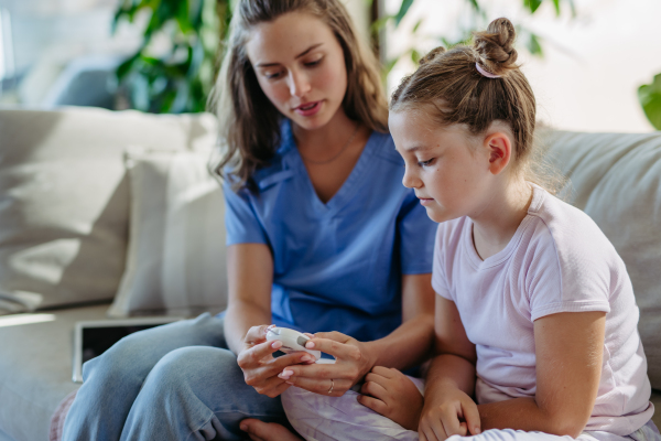 Nurse checking girl's blood glucose level using a fingerstick glucose meter. Endocrinologist waiting for results from blood test.