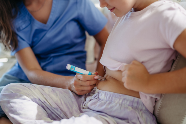 Nurse injecting insulin in diabetic girl belly. Close up of young girl with type 1 diabetes taking insuling with syringe needle.