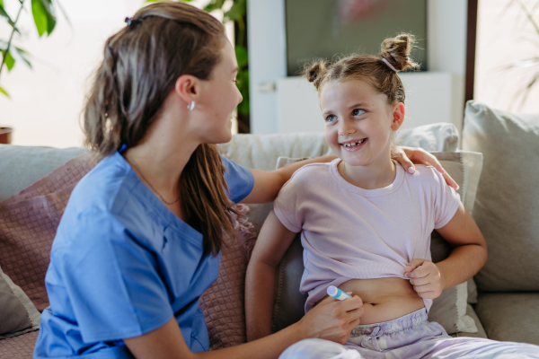 Nurse injecting insulin in diabetic girl belly. Close up of young girl with type 1 diabetes taking insuling with syringe needle.