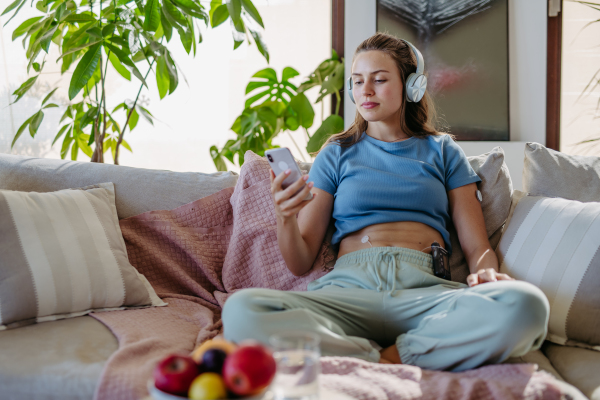 Diabetic woman with insulin pump and a continuous glucose monitor watching social media content on smart phone.The CGM device makes the life of the schoolgirl. easier, helping manage his illness and focus on other activities.