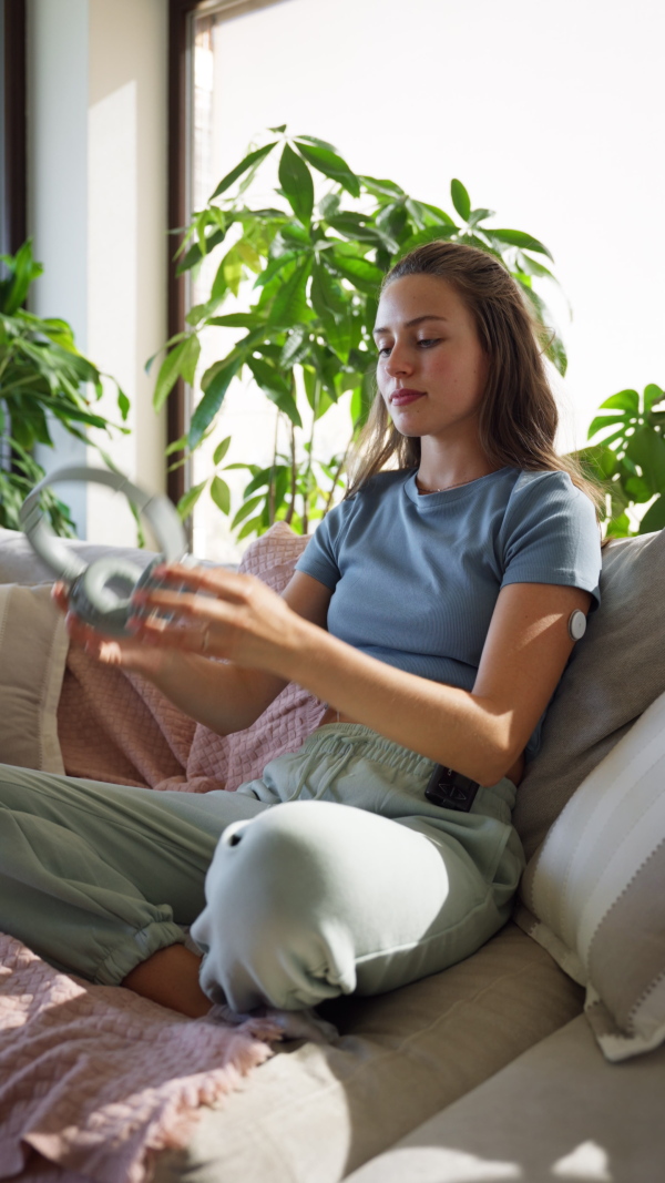 Diabetic woman with continuous glucose monitor sitting ondoors on sofa, watching social media content on smart phone.The CGM device makes the life of the schoolgirl. easier, helping manage his illness and focus on other activities.