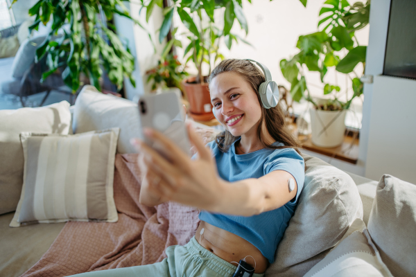 Beautiful diabetic girl taking a selfie, having an insulin pump and a continuous glucose monitor on her arm. Young woman is not ashamed of having diabetes, sharing her life with a chronic illness on social media.