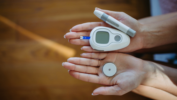 Close up of hands holding diabetes supplies and devices. Continuous glucose monitor, insulin pen, blood glucose meter. Banner with copy space.