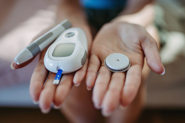 Close up of hands holding diabetes supplies and devices. Continuous glucose monitor, insulin pen, blood glucose meter. Banner with copy space.