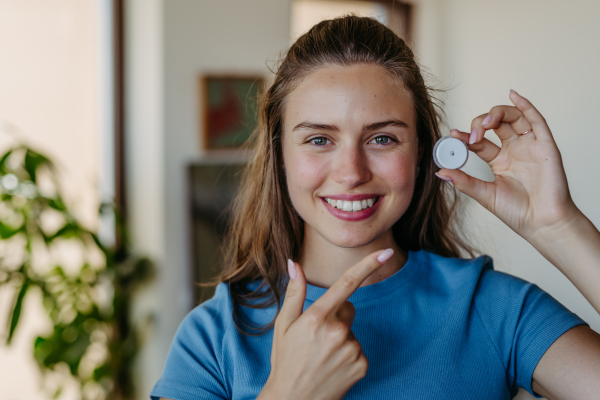 Portrait of beautiful diabetic girl pointing at continuous glucose monitor. Concept of life with chronic illness, diabetes.