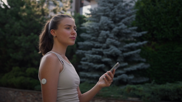 Beautiful diabetic woman preparing for outdoor workout in the city. Young woman with CGM checking her blood sugar level before exercising. Concept of exercise and diabetes.