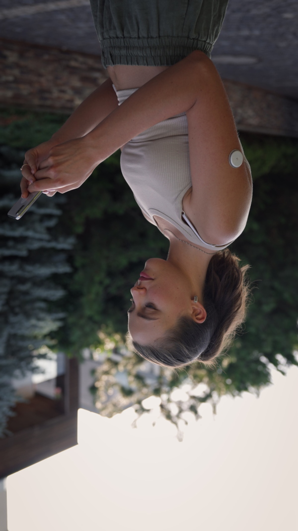 Beautiful diabetic woman preparing for outdoor workout in the city. Young woman with CGM checking her blood sugar level before exercising. Concept of exercise and diabetes.