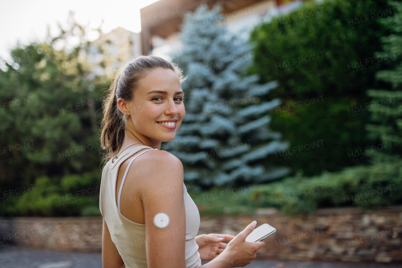 Beautiful diabetic woman preparing for outdoor workout in the city. Young woman with CGM checking her blood sugar level before exercising. Concept of exercise and diabetes.