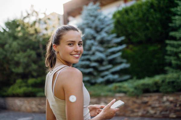 Beautiful diabetic woman preparing for outdoor workout in the city. Young woman with CGM checking her blood sugar level before exercising. Concept of exercise and diabetes.