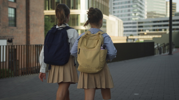 Rear view of two schoolgirls going to school. Classmates with backpacks in front of the school building.