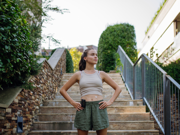 The beautiful diabetic woman preparing for outdoor run in the city. Young woman wearing an insulin pump during exercising. Concept of exercise and diabetes.