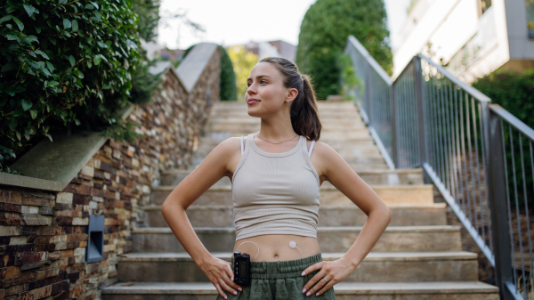 Beautiful diabetic woman preparing for outdoor run in the city. Young woman wearing an insulin pump during exercising. Concept of exercise and diabetes. Banner with copy space.