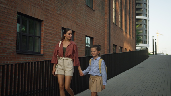 Front view of mother and little girl holding hands, going to school for the first time. The little schoolgirl is starting the first grade. Concept of back to school.