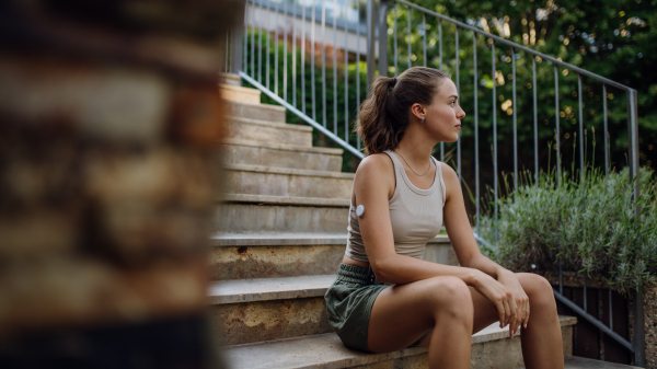 Beautiful diabetic woman preparing for outdoor run in the city. Young woman wearing continuous glucose monitor during exercising. Concept of exercise and diabetes. Banner with copy space.