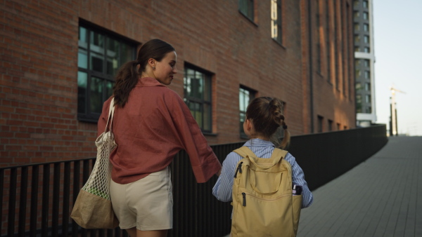 Rear view of mother and little girl holding hands, going to school for the first time. The little schoolgirl is starting the first grade. Concept of back to school.