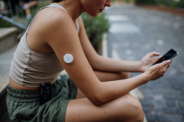 Beautiful diabetic woman preparing for outdoor workout in the city. Young woman with insulin pump and cgm, checking her blood sugar level before exercising. Concept of exercise and diabetes.