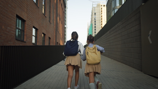 Rear view of two schoolgirls going to school. Classmates with backpacks in front of the school building.