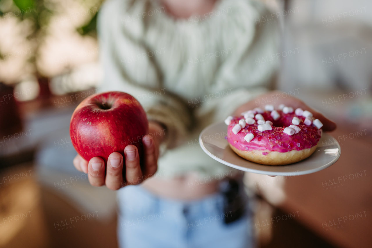 Diabetic woman is choosing between a fresh apple and a sweet doughnut. Importance of proper nutrition and diet in diabetes.