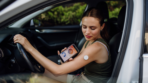 Woman with diabetes checking her blood glucose level before driving a car. Diabetic woman connecting CGM to a smartphone to monitor her blood sugar levels in real time.