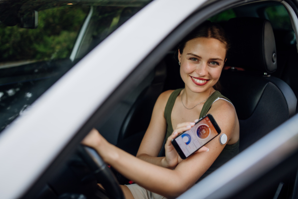 Woman with diabetes checking her blood glucose level before driving a car. Diabetic woman connecting CGM to a smartphone to monitor her blood sugar levels in real time.