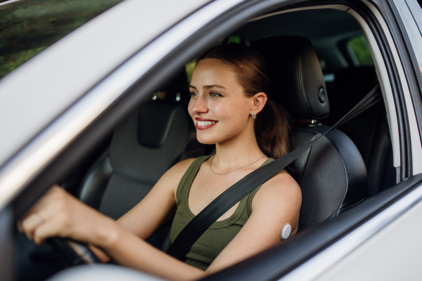 Woman with continuous glucose monitor driving car. Diabetic woman with CGM needs to raise her blood sugar level to continue driving car.