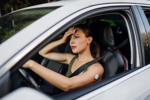 Woman with diabetes feeling dizzy during car drive. Diabetic woman with CGM needs to raise her blood sugar level to continue driving.