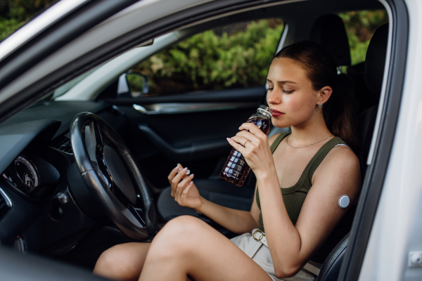 Woman with diabetes feeling dizzy during car drive. Diabetic woman with CGM needs to raise her blood sugar level to continue driving, drinking sweet drink.