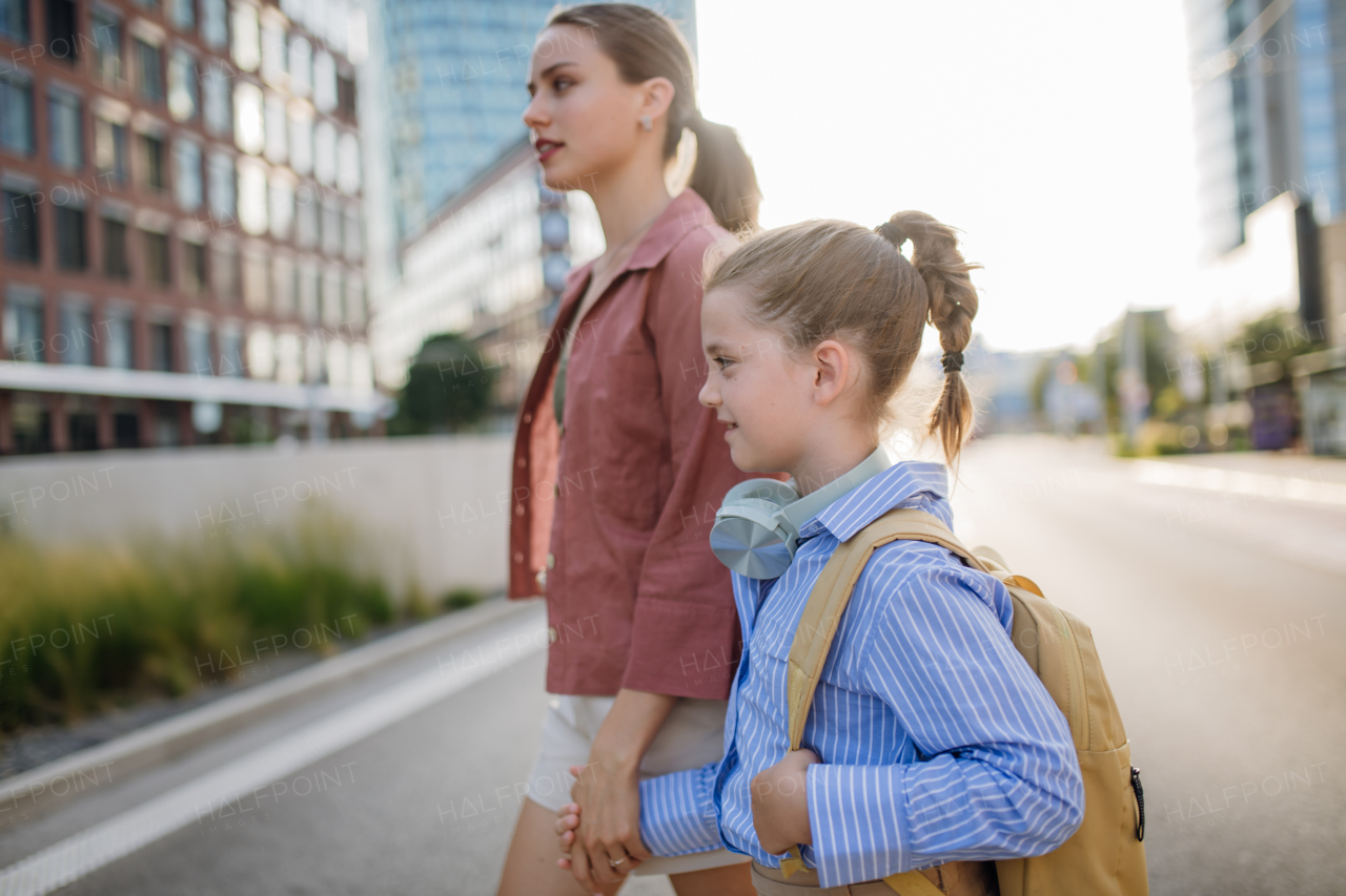 Rear view of mother and little girl holding hands, going to school for the first time. The little schoolgirl is starting the first grade. Concept of back to school.