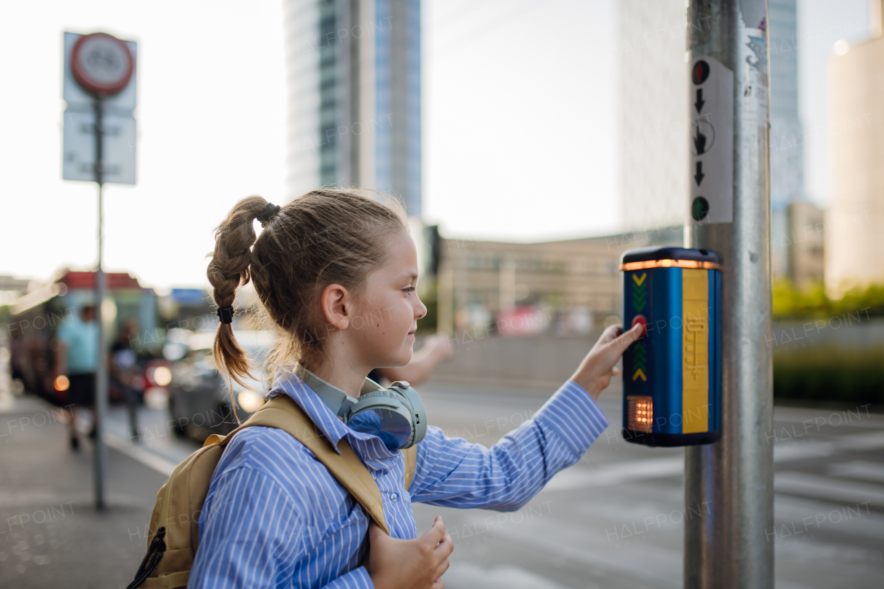 Young schoolgirl standing at the crosswalk and pressing the crosswalk button, waiting for the traffic light to turn green. Concept of back to school.