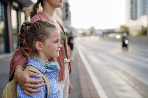 Mother and school girl with a backpack holding hands while crossing a busy road. Concept of back to school.