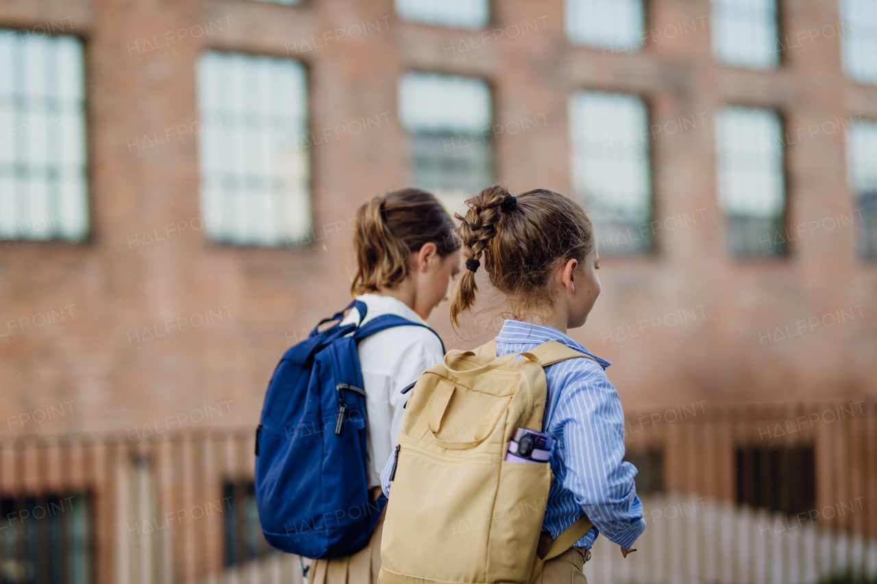 Rear view of two schoolgirls going to school. Classmates with backpacks in front of the school building.