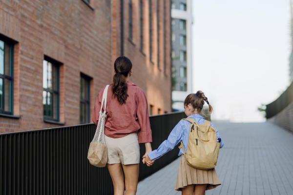 Rear view of mother and little girl holding hands, going to school for the first time. The little schoolgirl is starting the first grade. Concept of back to school.