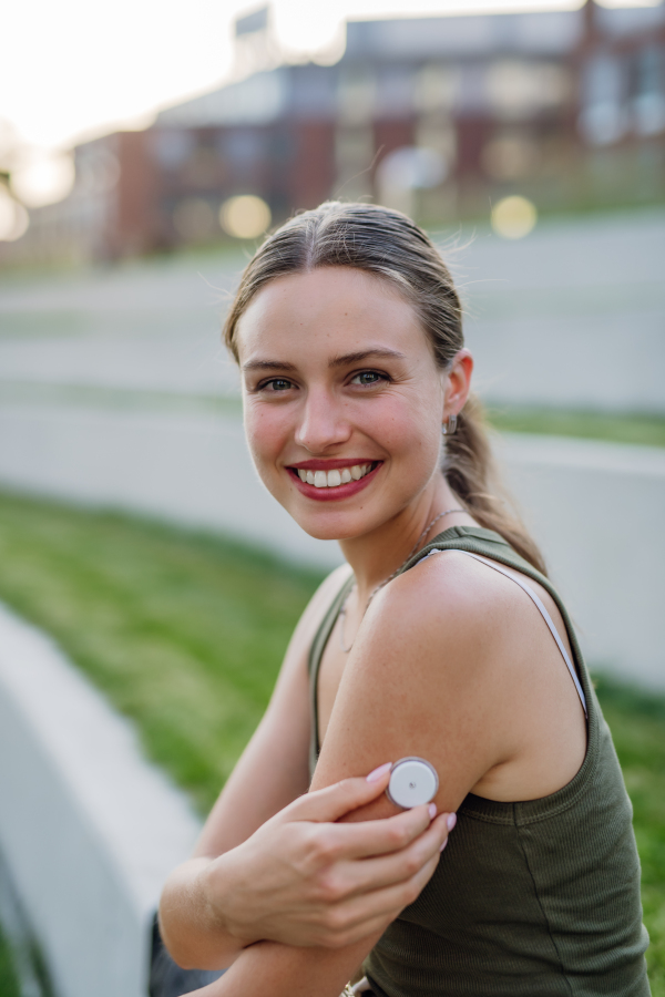 Portrait of beautiful diabetic woman with continuous glucose monitor on arm outdoors, in the city.