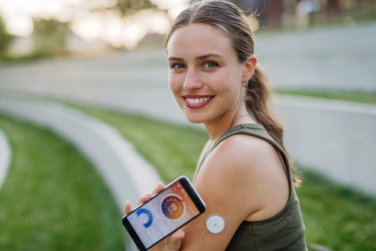 Woman with diabetes checking blood glucose level outdoors using continuous glucose monitor. Diabetic woman connecting CGM to a smartphone to monitor her blood sugar levels in real time.