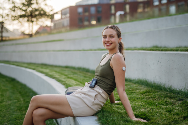 Portrait of beautiful diabetic woman with insulin pump and continuous glucose monitor on arm outdoors, in the city.