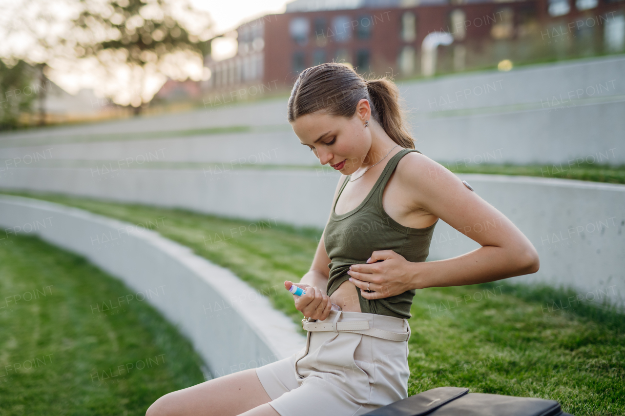 Woman injecting insulin in her abdomen outdoors, in park. Close up of woman with type 1 diabetes taking insuling with syringe needle.