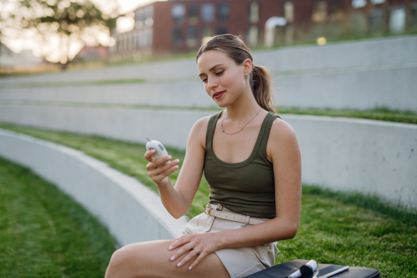 Diabetic woman checking her blood glucose level using a fingerstick glucose meter in public park. Waiting for results from glucometer blood test outdoors in city.