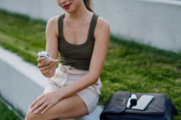 Diabetic woman checking her blood glucose level using a fingerstick glucose meter. Waiting for results from blood test outdoors.