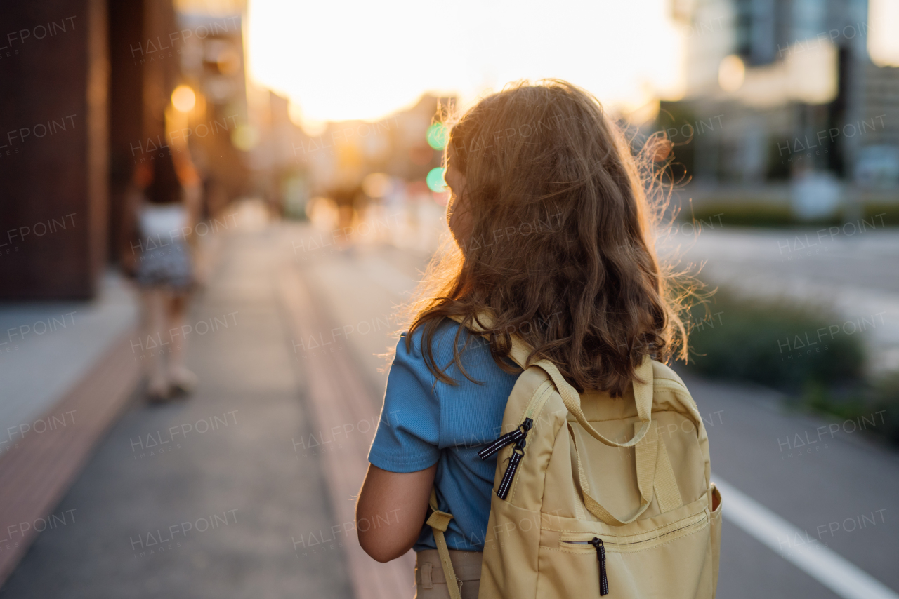 Rear view of a girl with a backpack goging to school in the morning. Schoolgirl returns home after a long day at school. Concept of back to school.