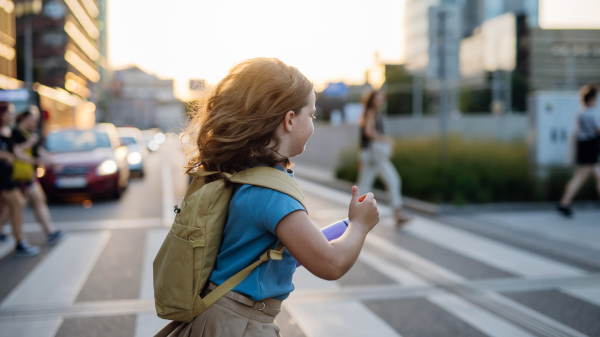 Side view of a girl with a backpack crossing the pedestrian crosswalk on her way to school. Concept of back to school.