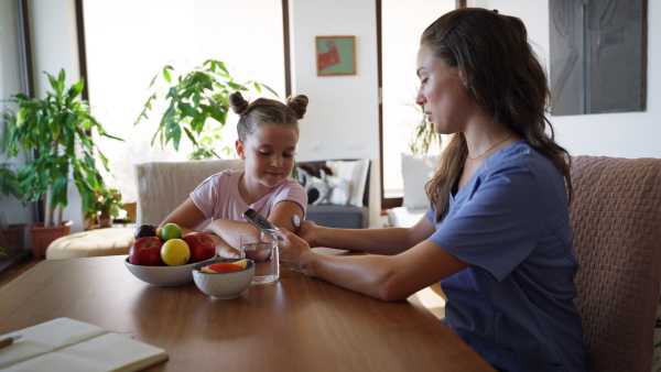 Girl with diabetes checking blood glucose level at home using continuous glucose monitor. Girl's mother connects CGM to a smartphone to monitor her blood sugar levels in real time.