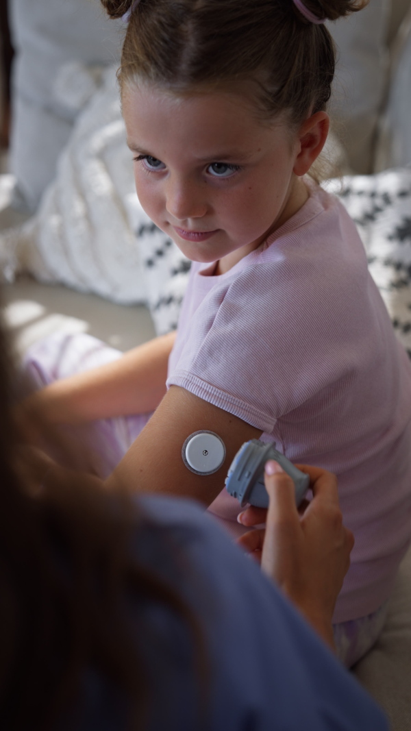 Nurse applying a continuous glucose monitor sensor to the arm of a diabetic girl. CGM device making life of school girl easier, helping manage his illness and focus on other activities.